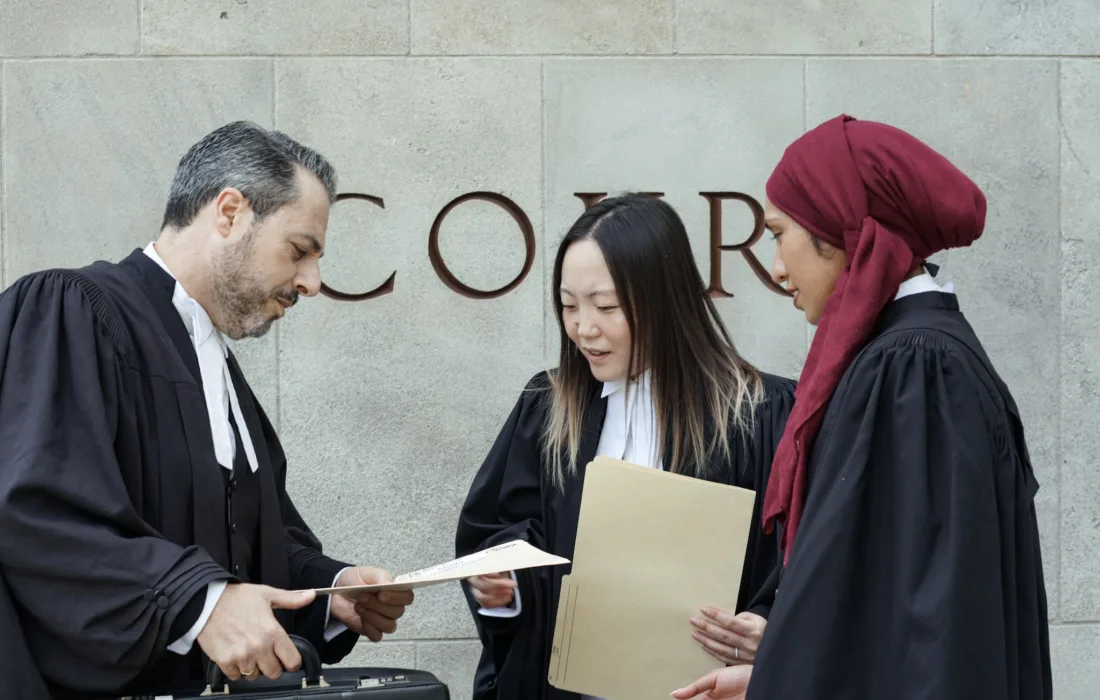 Three criminal defence lawyers exchanging notes outside a courthouse.